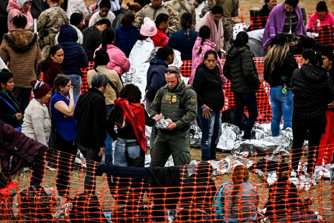 Un oficial de Aduanas y Protección Fronteriza de EE. UU. (C) da comida a inmigrantes que esperan ser procesados en un centro de tránsito de la Patrulla Fronteriza.