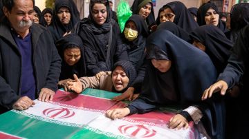 Una familia iraní está de luto junto a ataúdes envueltos con banderas iraníes durante la ceremonia fúnebre de la explosión.