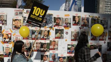 La gente camina junto a un muro con fotografías de rehenes durante una manifestación para conmemorar los 100 días que los rehenes han estado en cautiverio.