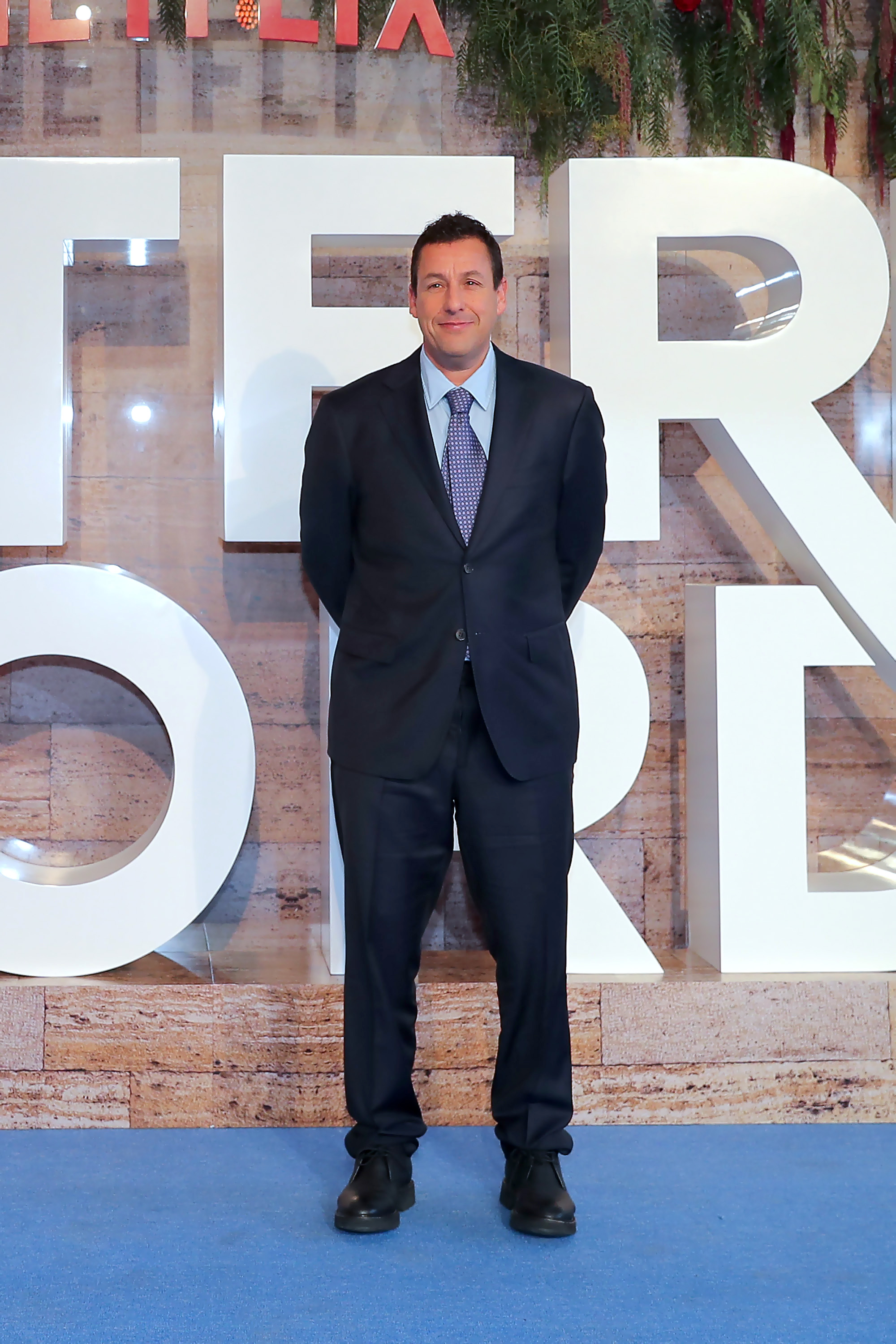 Adam Sandler posando en una alfombra roja.