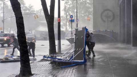 La gente intenta asegurar barreras destinadas a bloquear las aguas de inundación que fueron levantadas por el viento,