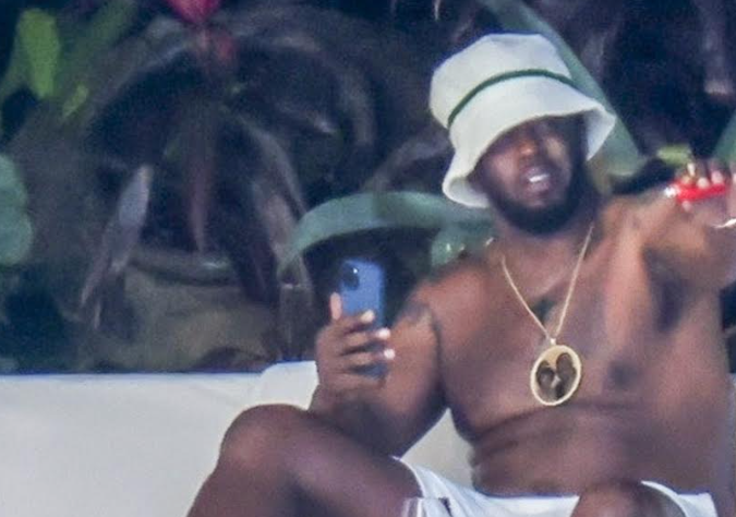 El rapero parece estar tomando una copa y fumando mientras descansa sin camisa con un sombrero de pescador.