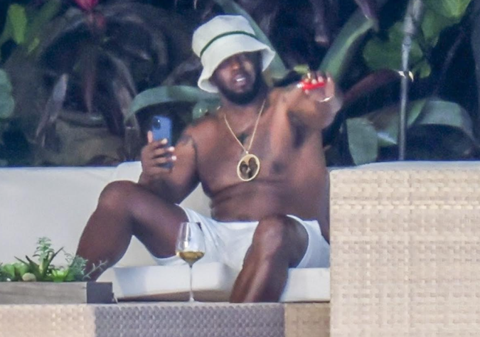 El rapero parece estar tomando una copa y fumando mientras descansa sin camisa con un sombrero de pescador.