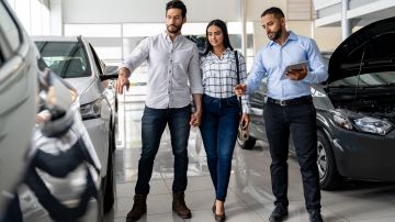 Latin American couple looking at cars at the dealership and talking to the salesman - business concepts