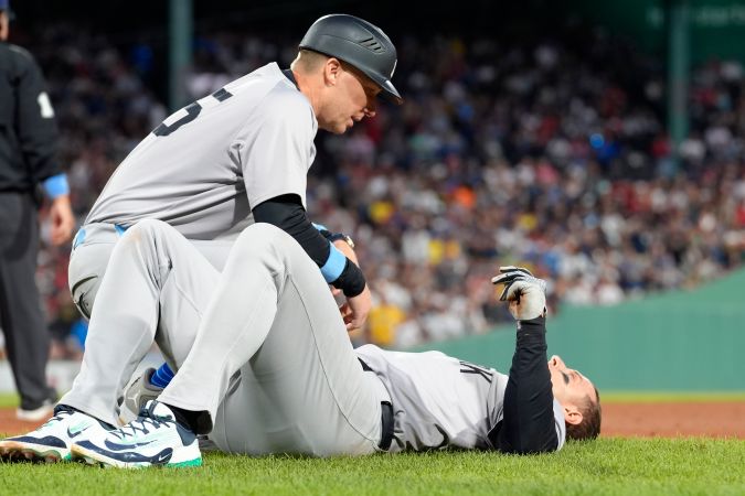 El entrenador de primera base de los Yankees de Nueva York, Travis Chapman, a la izquierda, atiende a Anthony Rizzo, a la derecha, luego de una colisión en la primera base en la séptima entrada de un juego de béisbol contra los Medias Rojas de Boston.
