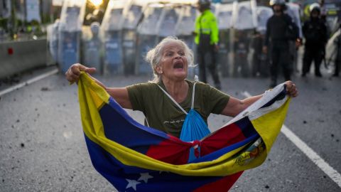 Consuelo Márquez sostiene una bandera venezolana frente a la policía que bloquea las manifestaciones contra los resultados oficiales de las elecciones.