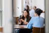 Mid adult female bank employee discusses a mobile banking app's features with a mature female client.