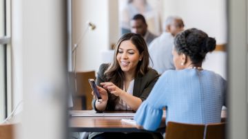 Mid adult female bank employee discusses a mobile banking app's features with a mature female client.