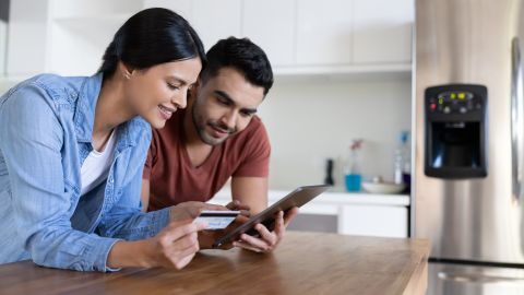 Happy Latin American couple shopping online from home using their tablet and paying by card