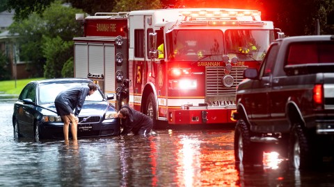 Varias personas atan un cable de remolque a un vehículo varado en una calle inundada después de las fuertes lluvias de la tormenta tropical Debby, el lunes 5 de agosto de 2024, en Savannah, Georgia.