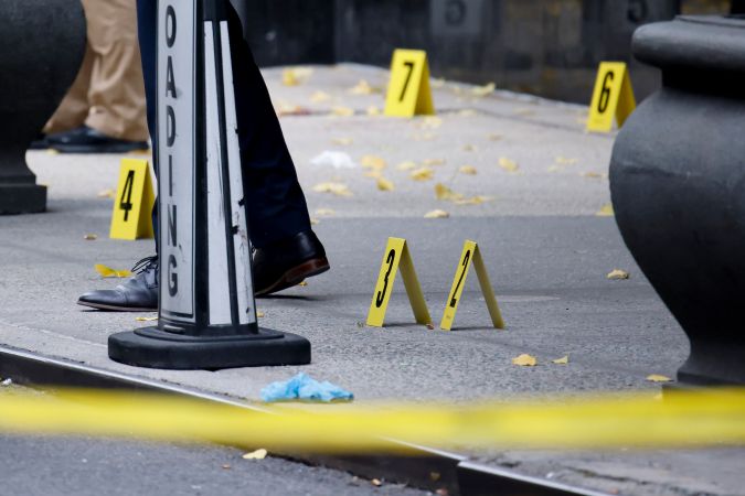 Miembros de la unidad de investigación de la escena del crimen de la policía de Nueva York investigan balas tiradas en la acera en el lugar de los hechos.