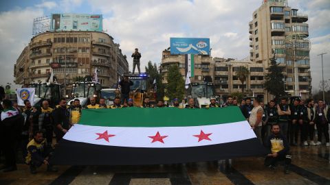 Miembros del grupo de Defensa Civil Siria, los Cascos Blancos, y otros voluntarios sostienen una bandera de la oposición siria durante una concentración para anunciar el inicio de la campaña de reparación en Alepo, Siria, el 25 de diciembre de 2024.