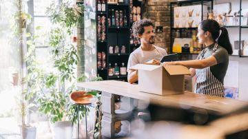 Female coffee roastery owner is busy packing an online order at the counter, while her colleague stands nearby having a chat.