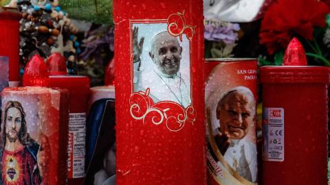 Una vela con la imagen del papa Francisco (centro) se coloca bajo la estatua de Juan Pablo II en el exterior del Hospital Agostino Gemelli, donde el papa Francisco permanece ingresado, en Roma, Italia, el 12 de marzo de 2025.