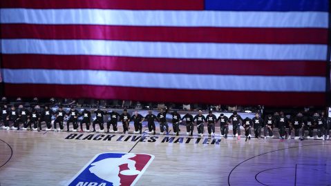 Jugadores del Orlando Magic y Brooklyn Nets se arrodillan ante un logo de Black Lives Matter durante el himno nacional en un encuentro en 2020. (AP Photo/, Pool, File)