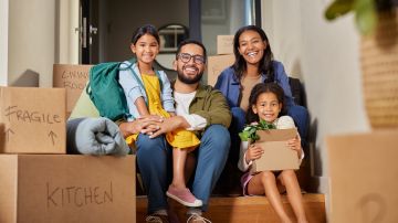 Middle eastern family sitting on stairs surrounded by moving boxes. Indian parents and their two daughters smiling on moving day. Mixed race family with daughters enjoy a moment of relax together during relocation.