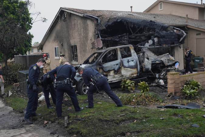 Policías investigan el área donde una camioneta fue impactada por la avioneta, causando más destrozos en una vivienda cercana.