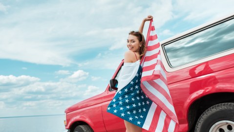 Happy,Beautiful,Girl,With,American,Flag,Standing,Near,Red,Car
