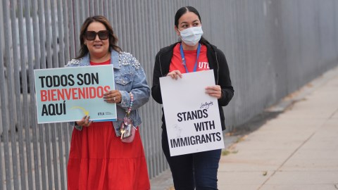 La maestra Nancy Barba (izquierda) y otro maestro sostienen carteles de apoyo a los inmigrantes el primer día de clases, el jueves 14 de agosto de 2025, en Los Ángeles.