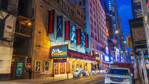 Fachada del Ambassador Theatre en Broadway, Nueva York, con marquesinas del musical Chicago iluminadas de noche.