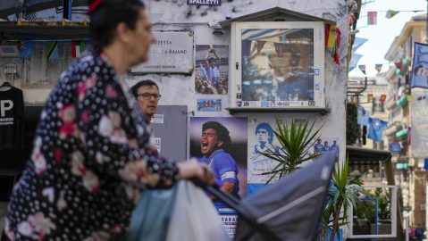 Una mujer empuja un cochecito de bebé junto a fotos de la leyenda del fútbol Diego Armando Maradona, en el centro de Nápoles, el 19 de abril de 2023.