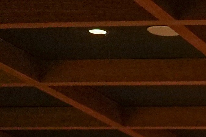 Interior del bar de KOBO en UNICO 20°105°, con estanterías iluminadas, botellas alineadas y sillas altas frente a una barra de madera.