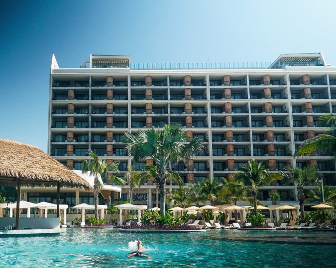 Fachada de UNICO 20°105° vista desde la piscina principal, con palmeras y camastros en el área exterior.