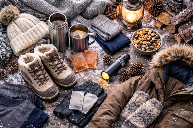 Ropa de abrigo, bebidas calientes y accesorios esenciales para soportar el frío extremo sobre una mesa con nieve.