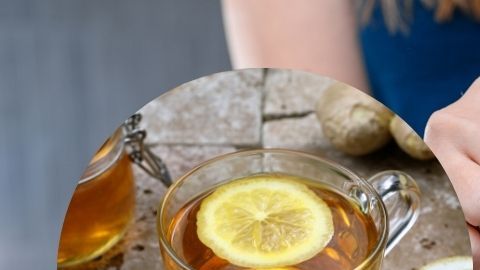 Una taza de infusiones calientes sobre una mesa de noche de madera, con ingredientes naturales como jengibre, limón y canela, en un ambiente nocturno relajado y acogedor.