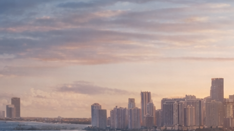 Empresario tecnológico camina frente a la costa de Miami con vista a mansiones y rascacielos.