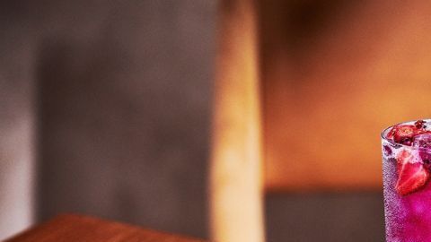 Vaso de Starbucks con bebida Pink Cannon Ball de color rosa vibrante, leche de coco, trozos de fruta de dragón y fresas sobre un fondo primaveral.