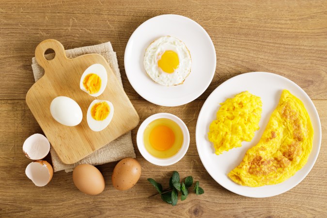 composición artística de huevos en diferentes cocciones: un huevo hervido a la mitad, un omelet esponjoso y huevos revueltos con vegetales sobre una mesa rústica.