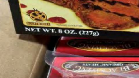 Dos bistecs New York Strip crudos, de corte grueso y con abundante marmoleado, están sazonados con sal gruesa y pimienta sobre un lote de productos.