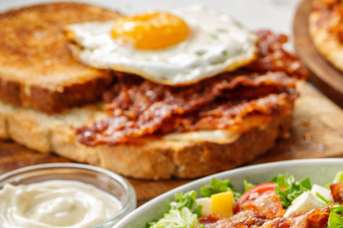 Ensalada con bacon crujiente acompañada de otros platos como huevo, tostadas y papa rellena