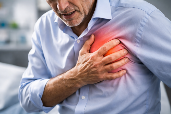 Hombre adulto con gesto de dolor llevándose la mano al pecho, posible síntoma de infarto o síndrome de corazón roto