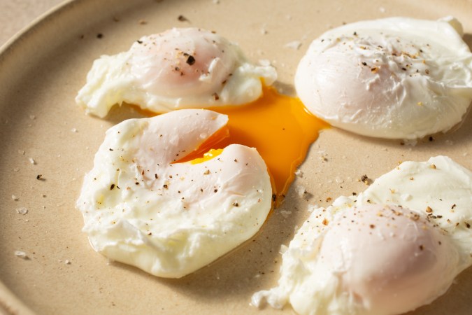 Cuatro huevos escalfados sobre un plato color arena en fondo blanco.