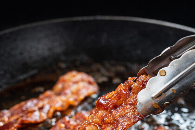 Persona cocinando bacon crujiente en una cocina luminosa en casa