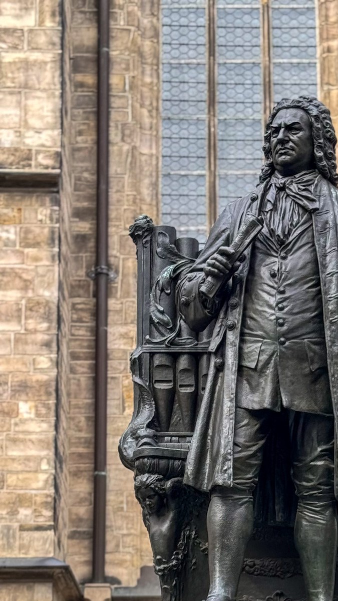 Estatua de bronce de Johann Sebastian Bach con un manuscrito en la mano frente a la fachada de la Thomaskirche en Leipzig