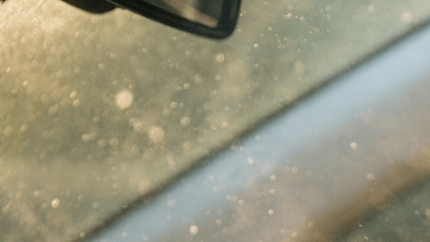 Mujer dentro de un carro reaccionando al mal olor del aire acondicionado con partículas visibles en el aire