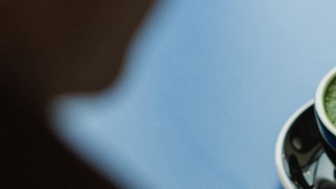 Hombre con medidor de glucosa en mano y una taza de café servido a un lado.