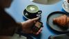 Hombre con medidor de glucosa en mano y una taza de café servido a un lado.