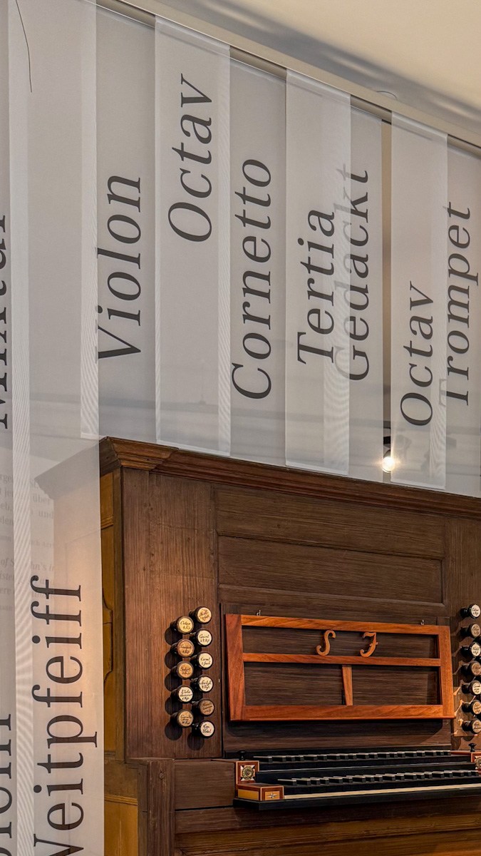Consola del órgano de madera proveniente de la antigua Johanniskirche de Leipzig, expuesta en el Bach-Museum, rodeada de cortinas con nombres de registros del órgano en alemán.