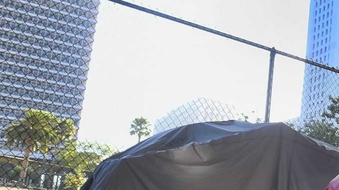 Un hombre sin hogar traslada sus pertenencias por una calle llena de carpas.