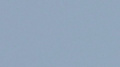 Dos hombres se sientan en una pequeña embarcación sobre el agua mientras buques de carga permanecen anclados al fondo en el estrecho de Ormuz.