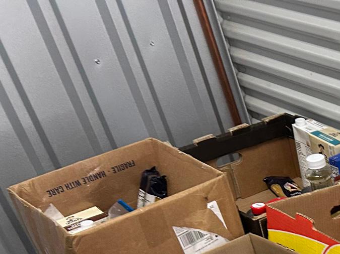 Boxes filled with various canned goods, cooking oils, and packaged food items stacked on a table in a storage facility.