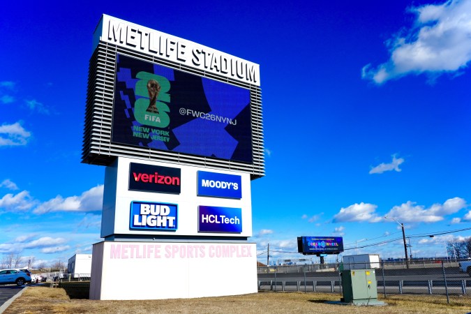 Letrero electrónico del MetLife Stadium muestra el logo de la FIFA y el hashtag @FWC26NYNJ promocionando el Mundial 2026 con cielo azul de fondo.