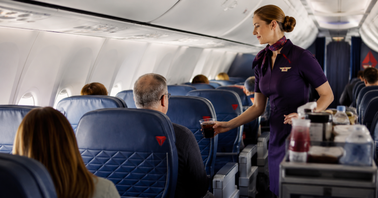 Interior de avión con azafata en pasillo y pasajeros sentados