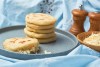 Pila de varias arepas, a un lado, una arepa con queso sobre plato gris y fondo azul.