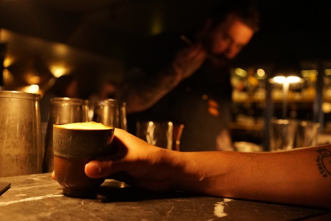 Cóctel con espuma servido en un vaso de cerámica en la barra de Copilote, con el bartender al fondo, en Hochelaga, Montreal