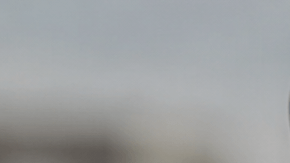 Mano sostiene un celular con una alerta sísmica en pantalla y edificios desenfocados al fondo.